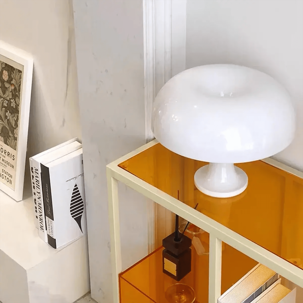 Unlit white mushroom lamp placed on a modern orange shelf beside books and decorative items